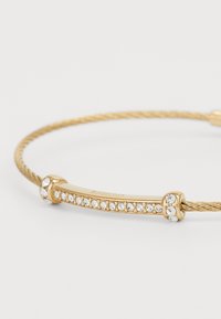 Bracciale in wire dorato con una barra liscia e curvata decorata con piccoli strass trasparenti e con estremità dettagliate.