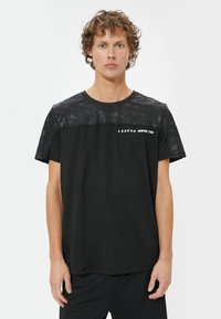 Sort t-shirt med en struktureret, camoflage-mønstret øverste sektion; har teksten "LEGEND INSIDE YOU." Kortærmet og med rund hals.