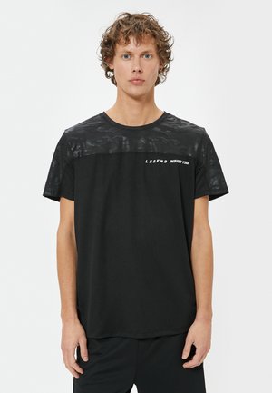 Sort t-shirt med en struktureret, camoflage-mønstret øverste sektion; har teksten "LEGEND INSIDE YOU." Kortærmet og med rund hals.