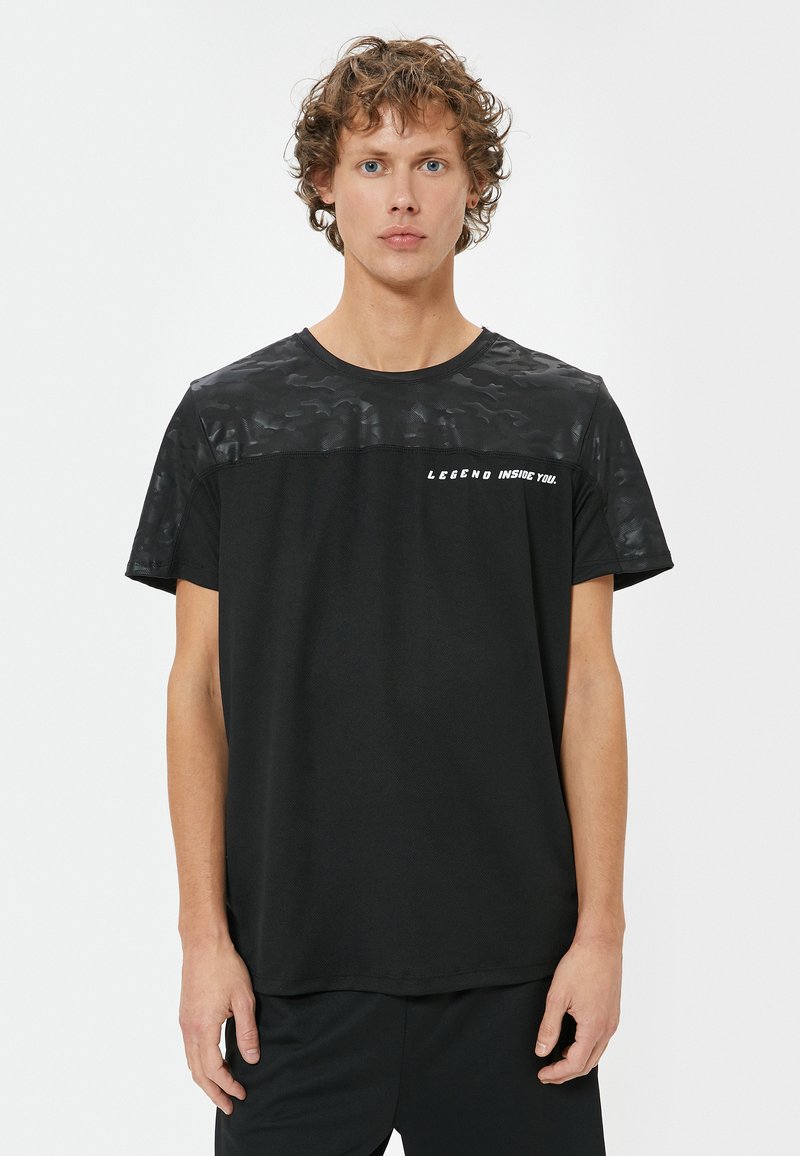 Sort t-shirt med en struktureret, camoflage-mønstret øverste sektion; har teksten "LEGEND INSIDE YOU." Kortærmet og med rund hals.