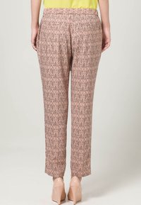 Kalhoty s elastickým pasem v růžovo-hnědém diamantovém vzoru, s bočními kapsami a rovnými nohavicemi, doplněné o béžové lodičky.