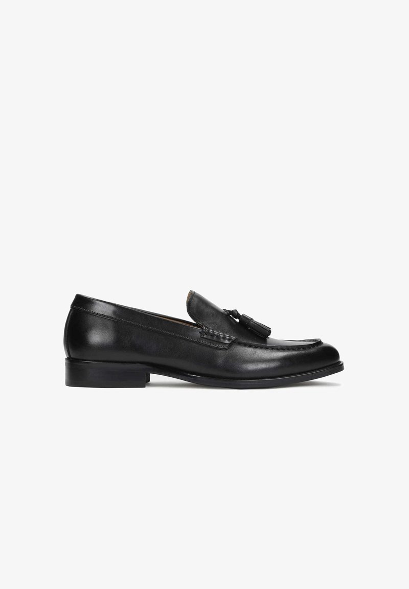 Mocassin en cuir noir à pampilles avec petit talon et détails cousus, présenté en profil latéral sur fond blanc.