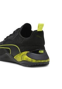 Chaussure de sport noire avec des accents de rayures jaunes, une languette jaune au talon et le mot "FUSE" sur la section de soutien du talon.