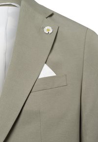 Helle graue Sakkajacke aus strukturiertem Stoff, ausgestattet mit einer Gänseblümchen-Reversnadel und einem weißen Taschentuch, das aus der Brusttasche hervorschaut.