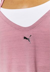 Osoba ubrana w różowy top w kształcie litery V z małym czarnym logo Pumy na środku oraz białą koszulką pod spodem widoczną przy dekolcie.