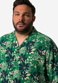 Camisa de manga corta verde con flores en azul oscuro y crema. Diseño con cuello y botones, hecha de una tela ligera.