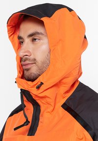Orange jacket with a black hood, featuring a high collar, adjustable drawstring, and a textured, weather-resistant fabric.