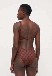Brown swimsuit with floral pattern, soft texture, wide straps, and a low back design. Features a clasp closure and gold branding.