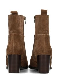 Stivali alla caviglia in suede marrone con punta arrotondata, cerniere laterali e tacco in legno impilato. Presentano una texture morbida e un design minimalista.
