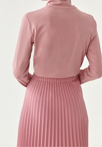 Dlouhý rukáv top a skládána sukně z jemné růžové tkaniny. Top má stojáček; sukně má vertikální sklady a přiléhavý pas.