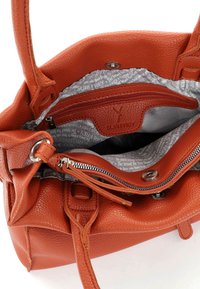 Orange texturerad läderhandväska med silverdetaljer. Inuti finns en grå foder med tryckt text, ett zipfack och magnetstängning.