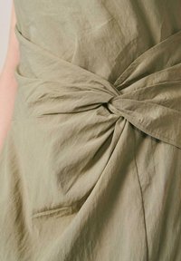 Primer plano de tela beige retorcida en un detalle de nudo en una prenda, destacando la textura y el drapeado.