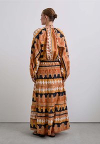 Robe maxi orange, noire et blanche avec un motif design. Manches longues et taille élastique avec des volants froncés sur la jupe.