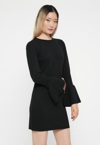 Čierne dlhé šaty s rozšírenými rukávmi, vyrobené z hladkej látky. Vybavené okrúhlym výstrihom a priliehavou siluetou. Jednoduchý a elegantný dizajn.