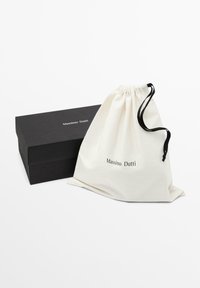 Boîte rectangulaire noire Massimo Dutti à côté d'une pochette blanche à cordon avec un cordon noir et le nom de la marque imprimé en noir.
