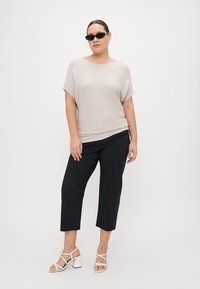 Beige svītrots adīts tops ar īsām piedurknēm, apvienots ar melniem potīšu garuma biksēm un baltām blokveida papēžu sandālēm. Aksesuāri ietver melnus saules brilles.