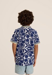 Korte mouwen polo shirt in blauw en wit met abstracte patronen, voorzien van een gestructureerde stof en een contrasterende kraag met gele accenten.