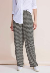 Lösa svarta och vita mönstrade byxor med elastisk midja, ihop med en vit skjorta med knappar och vita sneakers.