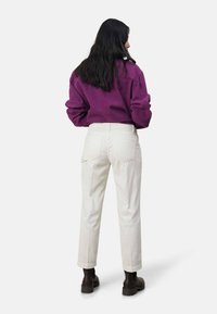 Fioletowa oversize'owa bluza i kremowe spodnie z kordurowej tkaniny z tylnymi kieszeniami, zestawione z ciemnymi botkami za kostkę. Gładkie tekstury i luźny krój.