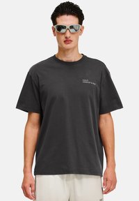 Svart bomullströja med kort ärm. Har en framsides-logga "HALO 19681972" i vitt. Modellen bär reflexiva solglasögon.