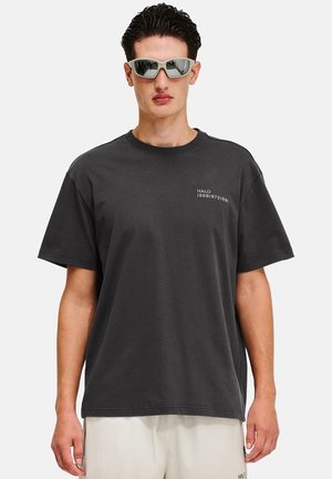 Sort bomulds T-shirt med korte ærmer. Har frontlogoen "HALO 19681972" i hvid. Modellen bærer reflekterende solbriller.