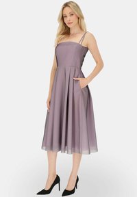 Lila sukienka w kształcie litery A z cienkimi ramiączkami, do kolan, rozkloszowany dół, boczne kieszenie i gładka faktura. Wzbogacona o czarne szpilki.
