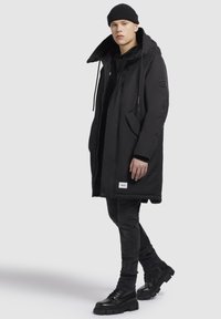 Czarna ocieplana parka z kapturem, zamkiem błyskawicznym i kieszeniami. Nosi się ją na czarnym hoodie, w połączeniu z czarnymi dżinsami i masywnymi czarnymi butami.