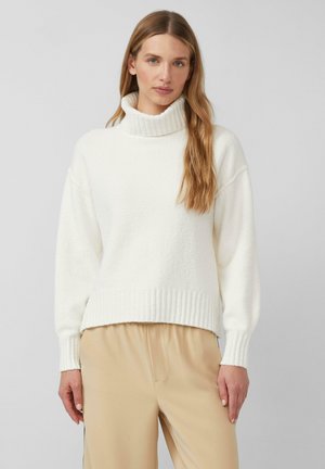 Cremfarbener Rollkragenpullover mit gerippten Abschlüssen und einem weichen, strukturierten Stoff. Leicht oversized Fit, kombiniert mit beigen Hosen.