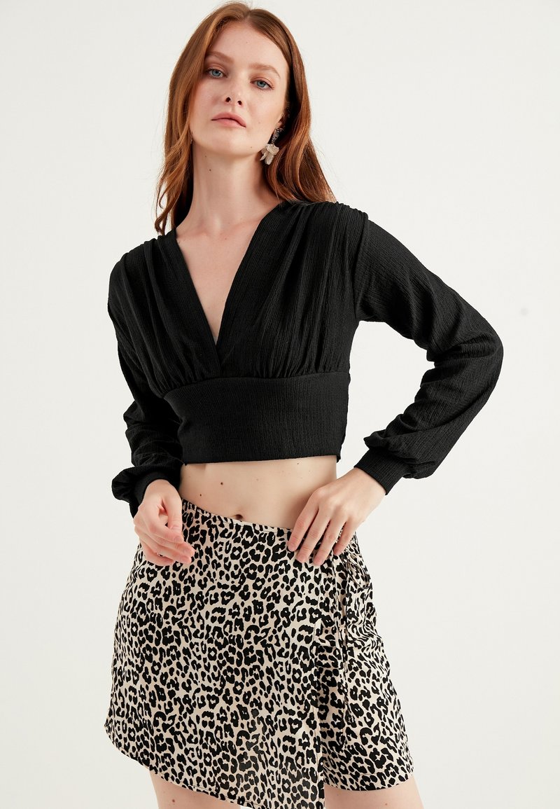 Crop top lungo nero con texture, maniche lunghe e scollatura profonda, abbinato a una mini gonna leopardata con orlo asimmetrico.