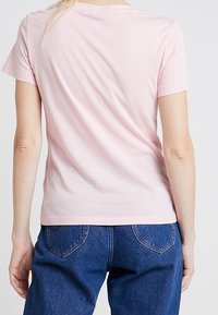 Camiseta de algodón de color rosa claro, con mangas cortas y un escote Redondo. Textura suave; la vista posterior resalta la simplicidad en el diseño.