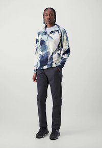 Multicolored pullover with a high collar, featuring abstract blue and green patterns, paired with dark pants and black athletic shoes.