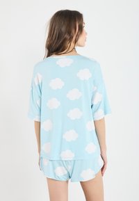 Set de pijama de culoare albastră deschisă, format dintr-o bluză lejeră și șorturi, decorate cu modele de nori albi. Material moale, cu mâneci scurte.