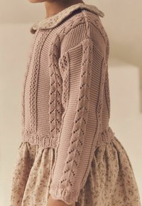 Pull en maille rose clair avec un motif texturé et un col floral, associé à une jupe à imprimé floral.