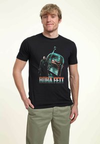 Černé tričko s grafikou Boba Fetta s metalickou helmou. Pod tímto je text "BOBA FETT" tučnými tyrkysovými a oranžovými písmeny.