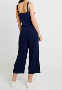 Námořnický pruhovaný pletený top s širokými ramínky, v kombinaci s odpovídajícími culotte kalhotami. Model má na sobě bílé tenisky. Hladká textura, uvolněný střih.