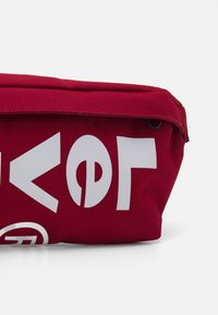 Trousse en tissu rouge avec des imprimés graphiques blancs, dotée d'une fermeture éclair et d'une texture durable. Design compact avec un fond plat.