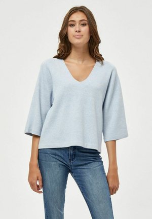 Helles blaues V-Ausschnitt-Oberteil mit weiten 3/4-Ärmeln, aus weichem Material gefertigt. Kombiniert mit Denim-Jeans. Schlichte, luftige Passform und minimalistisches Design.