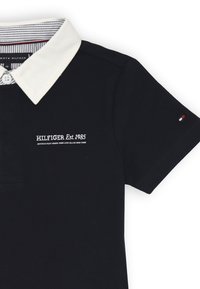 Polo nero realizzato in cotone. Caratterizzato da un colletto bianco, una fila di bottoni e un logo ricamato con "HILFIGER Est. 1985" in bianco.
