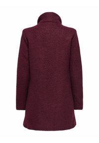 Burgundijas vilnas mētelis ar teksturētu apdari, ar augstu apkakli un garām piedurknēm, detaļveida šuvēm un vidus auguma garumu.