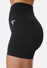 Pantalones cortos negros de cintura alta, fabricados con un tejido elástico, que presentan un ajuste ceñido y un pequeño logotipo blanco en el costado. Textura suave.