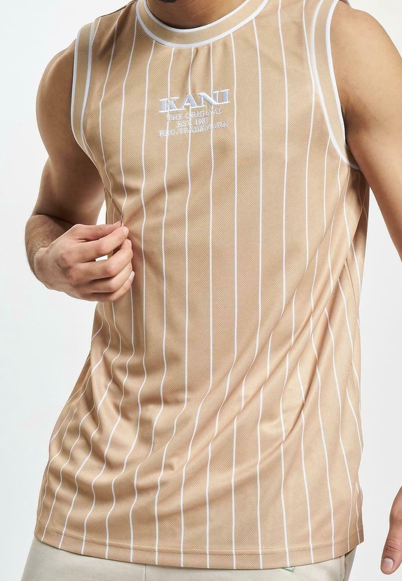 Beżowy, bezrękawnik z białymi pionowymi paskami. Posiada logo w białym tekście na klatce piersiowej. Wykonany z gładkiego, lekkiego materiału.