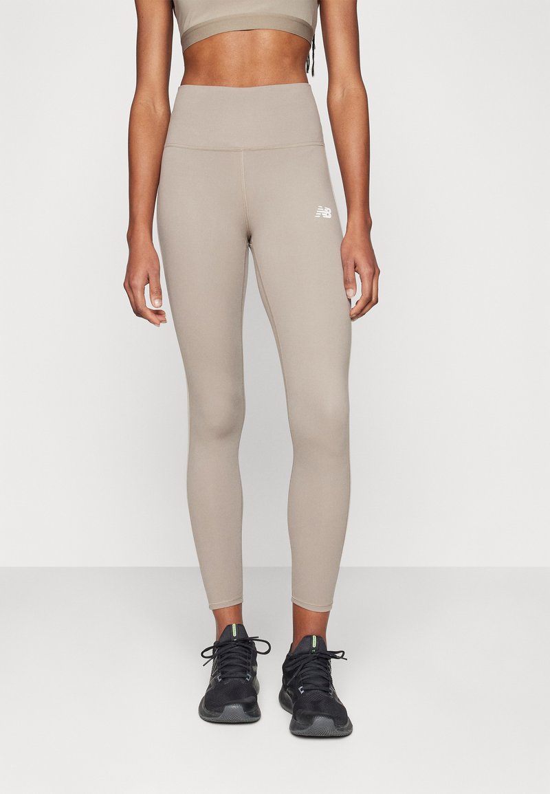 Leggings taille haute couleur brun clair en matière extensible, dotés d'un petit logo blanc sur la cuisse gauche et d'une texture lisse.