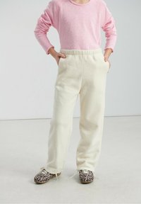 Pantalon en polaire crème avec une taille élastique et des poches, associé à un haut à manches longues rose pâle et des chaussures à motifs.