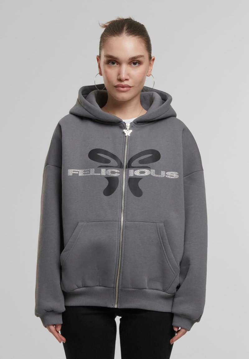 Grauer Reißverschluss-Hoodie mit einer Fronttasche, versehen mit einem großen schwarzen "FELICIOUS"-Logo und einem dezenten glänzenden Designelement. Weicher Stofftextur.