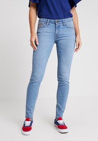 Jeans skinny de color azul claro hechos de denim, con un diseño clásico de cinco bolsillos y cierre de botón estándar, combinados con zapatillas rojas y azules.