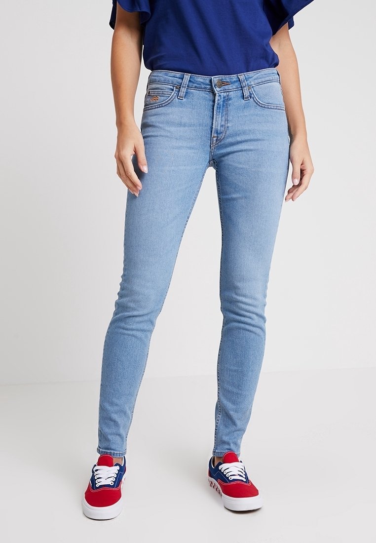 Jeans skinny de color azul claro hechos de denim, con un diseño clásico de cinco bolsillos y cierre de botón estándar, combinados con zapatillas rojas y azules.