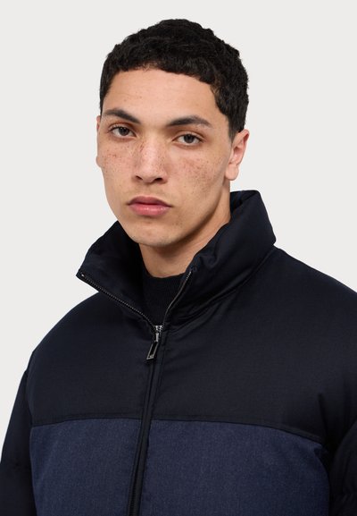 Dark, puffer jacket with high collar; features a color-blocked design in navy and deep blue; smooth texture; front zipper closure.