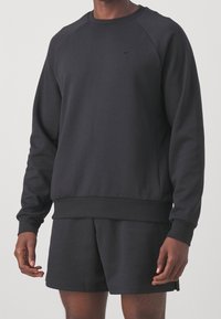 Homme portant un sweat-shirt à manches longues noir et un short assorti noir avec de subtils logos Nike sur la poitrine et la jambe.