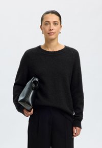 Suéter preto e felpudo com decote redondo e mangas compridas, combinado com uma elegante mala preta de couro com alça torcida.