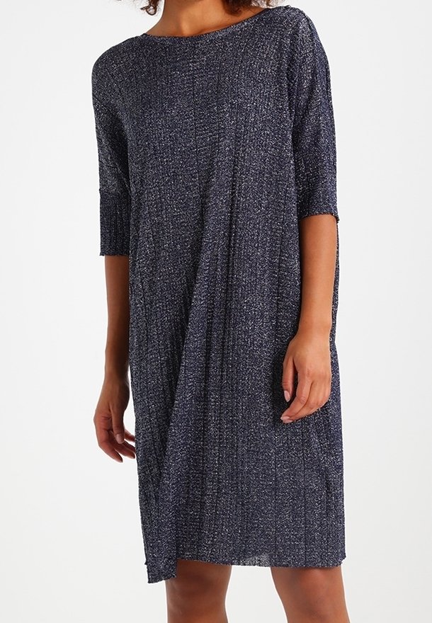 Femme portant une robe bleu foncé texturée, longueur genou, avec manches trois quarts et un col rond, sur un fond uni.